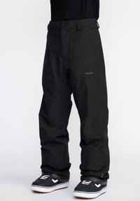 Pantalons de neige noirs imperméables avec une coupe décontractée, dotés d'une fermeture éclair, de passants de ceinture et d'un logo sur la cuisse. Tissu texturé pour plus de durabilité.
