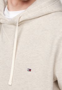 Beżowa bawełniana bluza z kapturem ze sznurkiem, z haftowanym logo w kolorach czerwonym, białym i niebieskim. Miękka tekstura i minimalistyczny design.