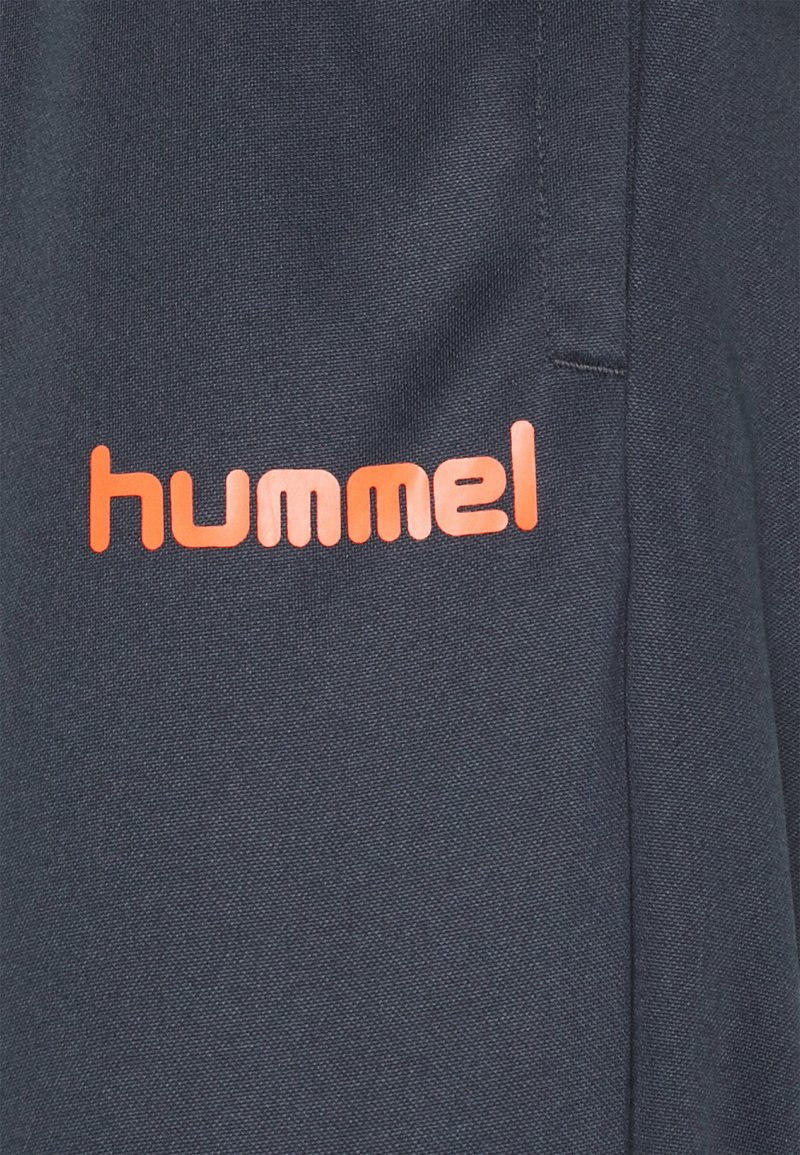 Pantalones deportivos navy de tejido suave, con un logo "hummel" naranja en el lado izquierdo y una textura lisa con costuras bien hechas.