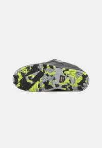 Black and gray sneaker sole with bright yellow and gray camo pattern. Features textured rubber for grip and a red logo tag at the center.
