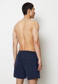 Shorts da nuoto color navy in tessuto leggero, con tasca posteriore e vita elastica per maggiore flessibilità. Texture liscia, lunghezza sopra il ginocchio.