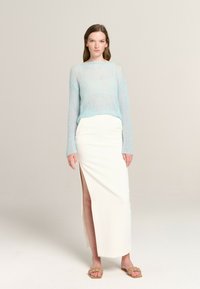 Light blue, sheer knitted sweater with long sleeves paired with a white high-slit skirt and beige braided slide sandals.