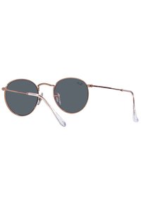 Occhiali da sole tondi con una sottile montatura in metallo color oro rosa. Lenti grigie e puntali trasparenti. Design minimalista con un focus su linee slanciate.