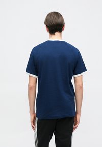 Námornícky modré bavlnené tričko s okrúhlym výstrihom a bielym lemovaním na rukávoch a golieri. Ľahké, voľné strih, s jednoduchým dizajnom bez vzorov.