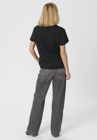 Čierne tričko s krátkym rukávom v kombinácii s vysokým pásom, širokými šedými džínsami. Tkanina vyzerá mäkko, s viditeľnými švy na džínsach.