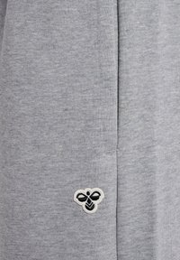 Der graue Sweatshirtstoff hat eine dezente Textur und ein kleines schwarz-weißes Bienenlogo ist am unteren Bereich eingestickt.