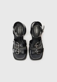 Sandalias negras con suela plana, diseño de múltiples correas con hebillas plateadas y correa en el tobillo. Fabricadas de material sintético suave.