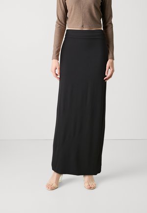 Black, floor-length skirt in smooth, stretchy fabric. Features a high waistband and falls straight with a simple design. Transparent heels visible.