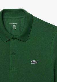 Polo verde de Lacoste con tejido texturizado, tapeta de dos botones y logo de cocodrilo bordado en el lado izquierdo del pecho. Ajuste regular.