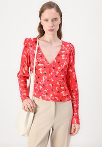 Röd blommig långärmad topp med V-ringning, med puffärmar och svarta detaljer, kombinerad med beige lösa byxor.