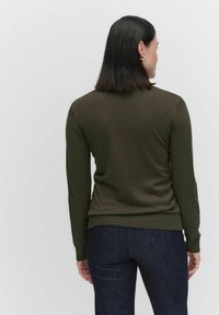 Mörkgrön tight passande tröja med långa ärmar, ribbade manschetter och nederkant; har en vertikal sömdetalj på baksidan. Matchad med mörka jeans.