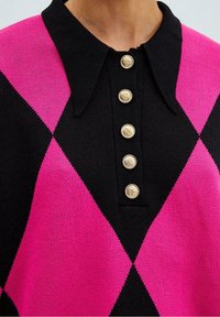 Schwarzer und pinker Pullover mit Rautenmuster, einem Kragen und fünf goldenen Knöpfen mit Emblem-Details an der Vorderseite.