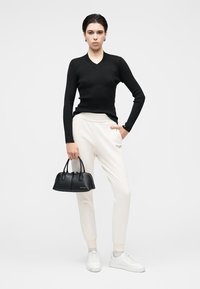 Μαύρο ριμπ πλεκτό μακρυμάνικο τοπ, εκρού παντελόνι jogger, λευκά αθλητικά παπούτσια, κρατώντας μαύρη τσάντα χειρός με διπλές λαβές, γκρι λεπτομέρειες στα παπούτσια.