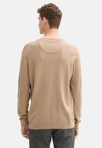 Suéter color marrón claro con mangas largas y cuello redondo, que cuenta con una textura suave y delicada, y un ajuste relajado. Diseño simple y clásico.