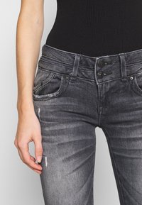 Jeans de mezclilla negros de tiro alto con un diseño deslavado, que cuentan con un cierre de doble botón y bolsillos frontales. Presenta pequeños detalles desgastados.