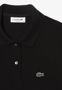 Polo noir avec un col à côtes et une patte de boutonnage à trois boutons. Présente un logo de crocodile brodé en vert sur la poitrine gauche.