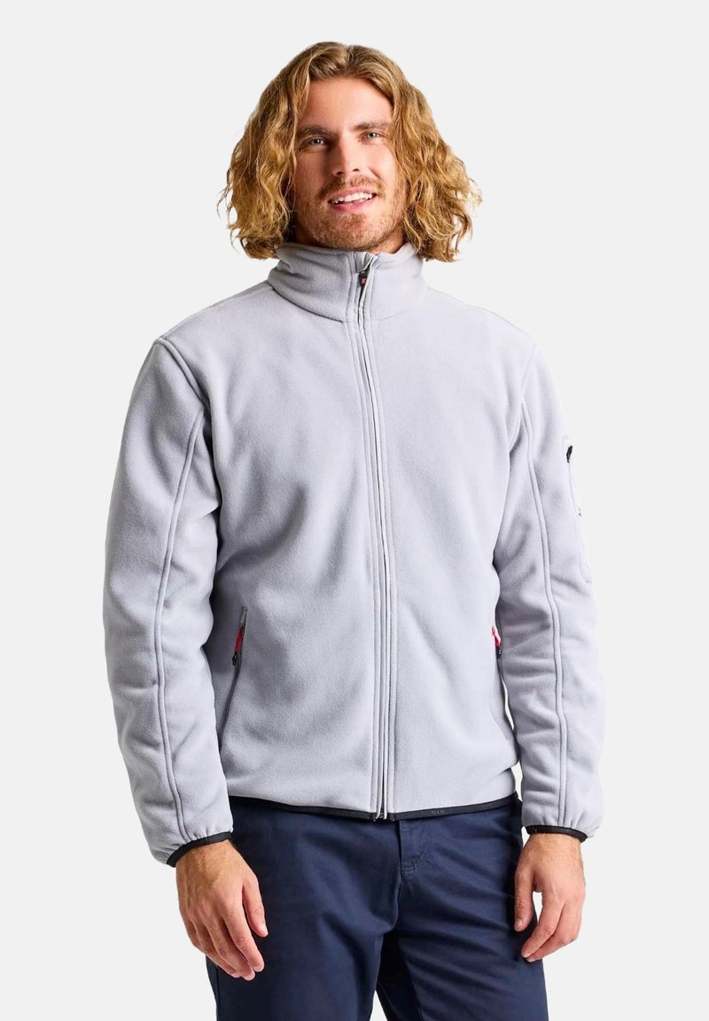 Giacca in pile grigio chiaro con colletto alto, zip frontale e tasche laterali con zip. Presenta accenti a contrasto sui polsini.