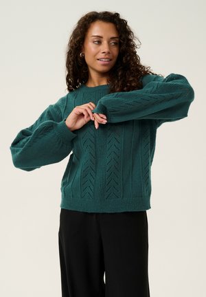 Teal knitted sweater with a textured pattern, featuring zigzag and ribbed designs. Loose-fitting with wide sleeves and a crew neck.