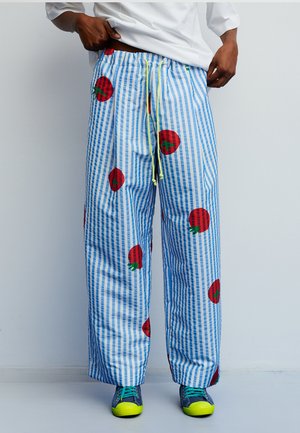 Szerokie spodnie w niebiesko-białe paski z czerwonymi wzorami pomidorów, wyposażone w elastyczną talię i żółty sznurek do regulacji.