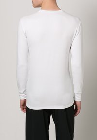 Camisa branca de manga longa feita de tecido suave, com decote redondo e design ajustado, vista de costas.