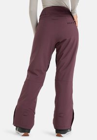 Burgundské sněhové kalhoty s vysokým pasem, nastavitelným pasem, bočními zipy a hladkým povrchem, vhodné pro zimní sporty.