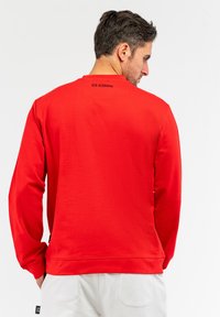 Rød bomulds sweatshirts med lange ærmer og rund hals. Har ribstrikkede manchetter og kant, samt et lille sort logo ved den bageste halsudskæring.