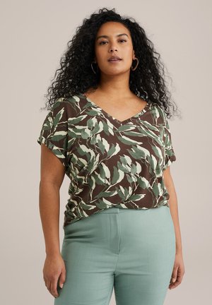 Bruine V-hals top met een bladgroen patroon, korte mouwen en een relaxte pasvorm. Gecombineerd met lichtblauwe tapered broeken. Soepele textuur.