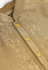 Kurta beige traditionnelle avec broderies dorées complexes, sequins, tissu à motifs et trois boutons jaunes sur la patte de boutonnage devant.