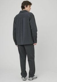 Chemise noire à manches longues et col, associée à un jogging assorti. Design simple avec coupe droite et minimalisme dans les décorations.