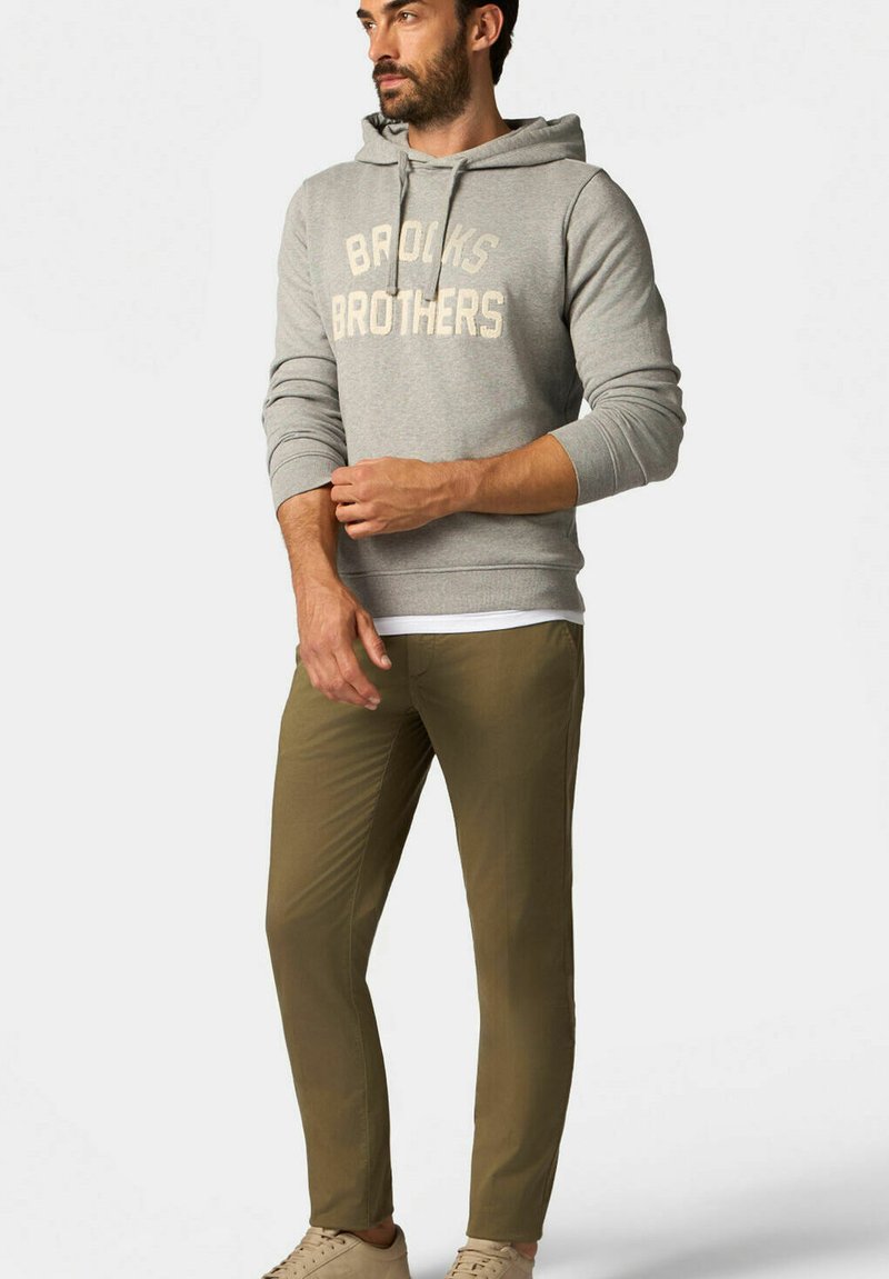 Felpa grigia con cappuccio con testo "Brooks Brothers", abbinata a pantaloni slim-fit verde oliva e sneaker beige. Tessuto di cotone morbido, design casual.