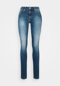 Jeans pitillo hechos de mezclilla azul, con un lavado medio con desvanecimiento, cinco bolsillos, cierre de botones y detalles de costura estándar.