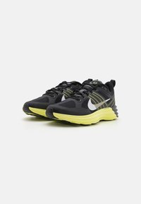 Fekete sportcipők textúrált felsőrésszel, lime zöld talppal, fehér swoosh logóval és sárga csíkokkal az oldalán. Kerek fűzők és párnázott boka rész.