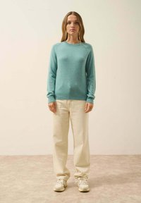 Pull bleu clair au toucher doux, col rond et ourlet côtelé, associé à un pantalon ample de couleur crème et à des baskets grises.