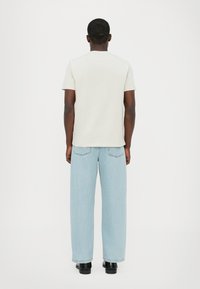 Lys grå kortermet t-skjorte og vide lyseblå jeans, sett bakfra, med svarte sko. Minimalistisk design og myk tekstur.