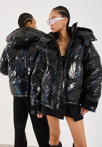 Black padded puffer jacket with shiny, reflective material. Features a hood, front pockets, and a cropped design with quilted detailing.
