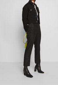 Černá zkrácená džínová bunda s dvěma náprsními kapsami, v kombinaci s přizpůsobenými černými kalhotami a černými botami na vysokém podpatku. Doplněk: malá jasně zelená taška.