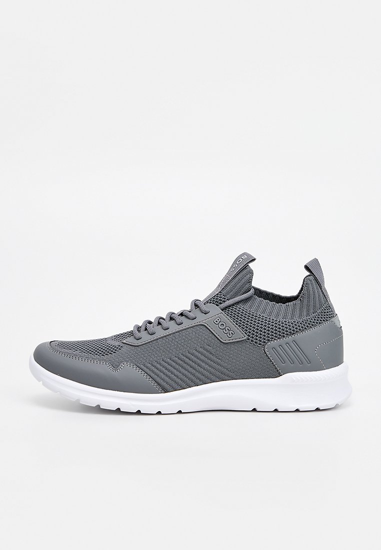 Zapatillas deportivas grises con parte superior de malla de textura acanalada y detalles lisos, suela de goma blanca y diseño de punta redondeada.