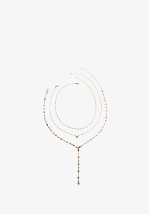 Zlatý vícevrstvý náhrdelník s třemi řetízky: jeden ve tvaru srdce, jeden propojovaný design a jeden s kapkovým závěsem s malými akcenty.