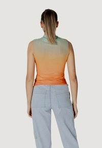 Top senza maniche con un gradiente dal verde menta all'arancione, realizzato in tessuto leggero. Abbinato a pantaloni cargo blu chiaro con tasche.