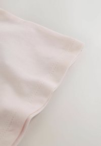 Material roz deschis cu textură moale, având tiv curbat și cusături albe contrastante de-a lungul marginii.