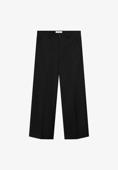 Sorte bukser med vide ben lavet af et glat materiale, med forlommer, knaplåsning og en presset rille ned langs hvert ben.