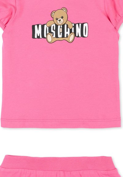Tenue rose pour tout-petit avec un motif d'ours en peluche serrant le texte "Moschino" sur le haut et pantalon assorti avec ceinture côtelée rose.