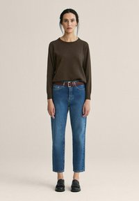 Ruskea pitkähihainen neulepaita, siniset korkeavyötäröiset farkut vaalealla pesulla, punottu ruskea vyö ja mustat loaferit. Yksinkertainen muotoilu, rento istuvuus.