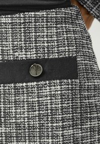 Tessuto tweed bianco e nero con un motivo texturizzato. Presenta una vita nera e un bottone decorativo argentato sulla tasca anteriore.