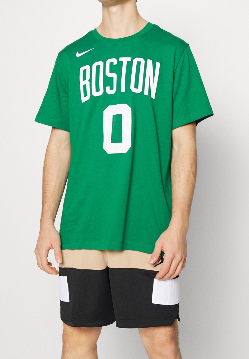 Zelené bavlněné tričko s nápisem "BOSTON" a číslem "0" vytištěným bíle. Má krátké rukávy. Kombinováno s béžovými a černými šortkami s kapsami.