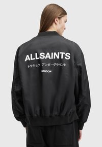 Crna bomber jakna sa satenskim završetkom, s velikim bijelim natpisom 'ALLSAINTS' i japanskim tekstom na leđima. Elastične manžete i rub.