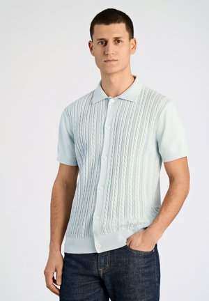 Cardigan tricot à manches courtes bleu clair avec un motif en cable, boutons sur le devant et accents côtelés le long du col et de l'ourlet.