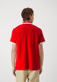 Camisa polo roja con cuello y acentos en las mangas blancos, hecha de algodón, con un diseño limpio y un corte profesional, exhibida desde la parte posterior.