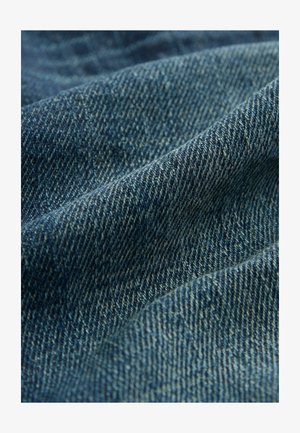 Denim fabric in dark blue hues with visible texture and weave patterns, showing soft folds and subtle variations in color.