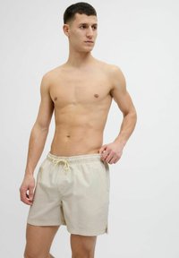 Lyse beige svøm shorts med et struktureret mønster, elastisk talje og snor. Knælængde design med sideslidser for let bevægelse.